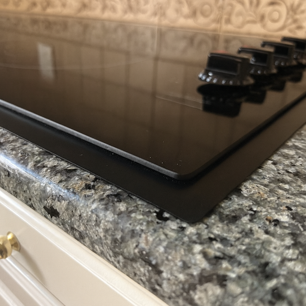 Close-up view of custom trim kit installed on black glass cooktop set into a granite countertop